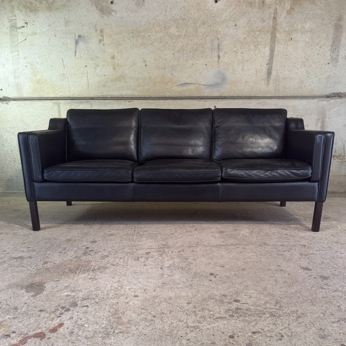 Black leather sofa in a room with concrete floor and wall.