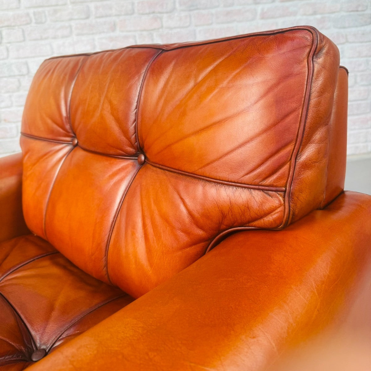 Brown leather sofa against a white brick wall.