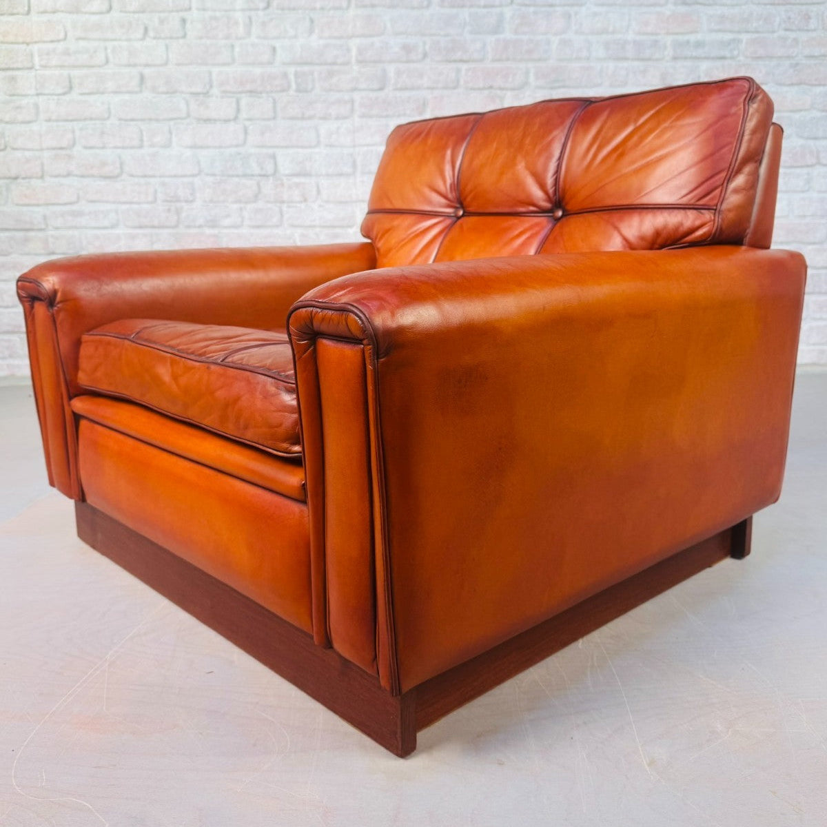 Brown leather armchair against a white brick wall.