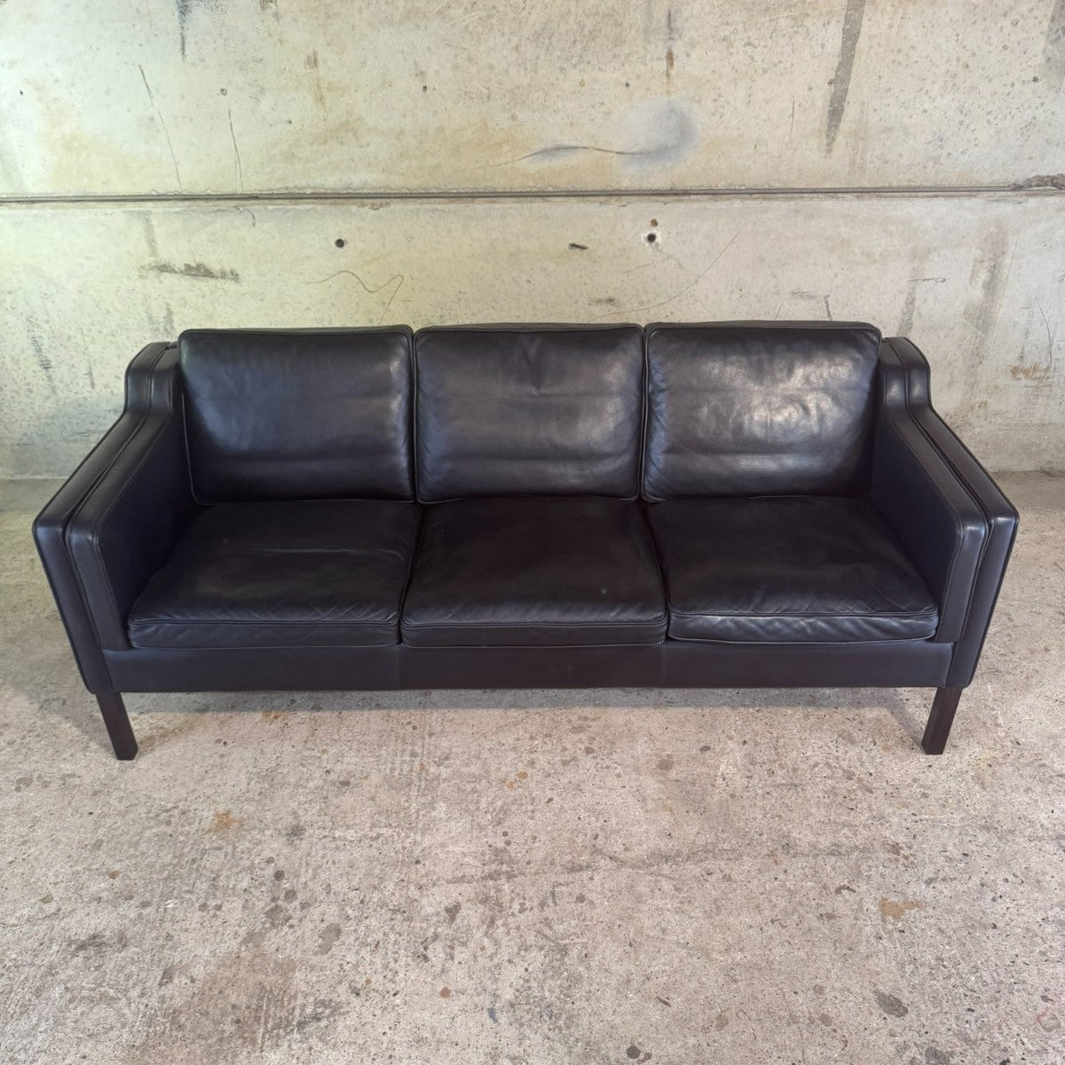 Black leather sofa against a concrete wall.